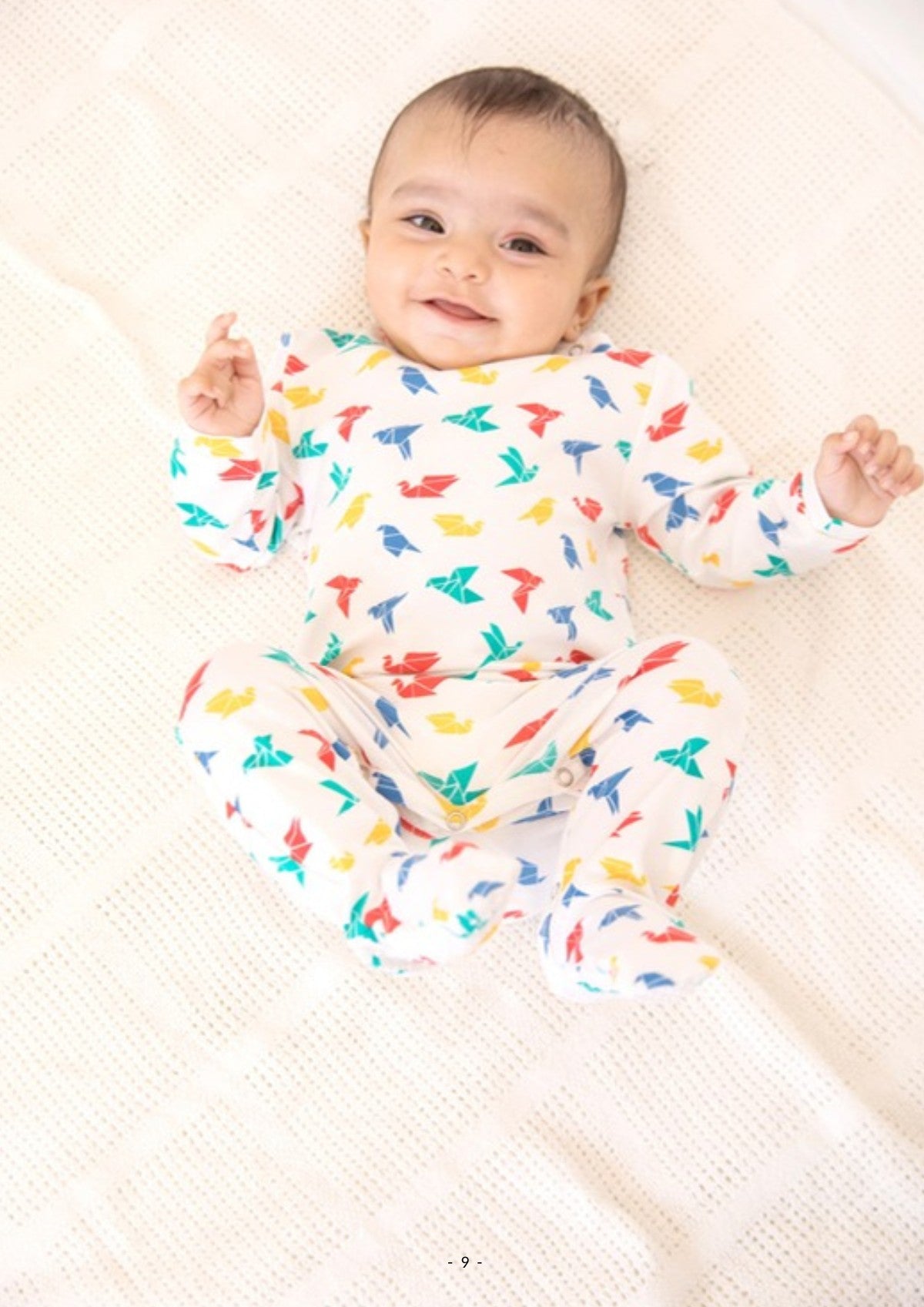 Smiling baby in an Ola! Otter organic cotton footed sleepsuit in a bird print
