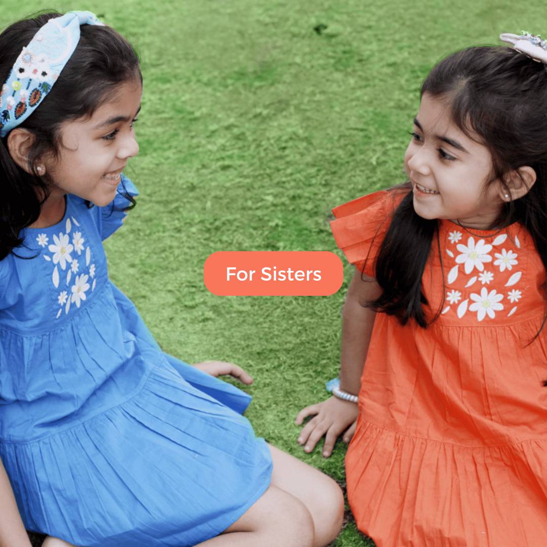 An image of two young girls happily wearing matching organic cotton dresses from Twining Sisters. The dresses feature a charming floral pattern with vibrant colors, embodying eco-conscious and stylish clothing great for gifting sisters